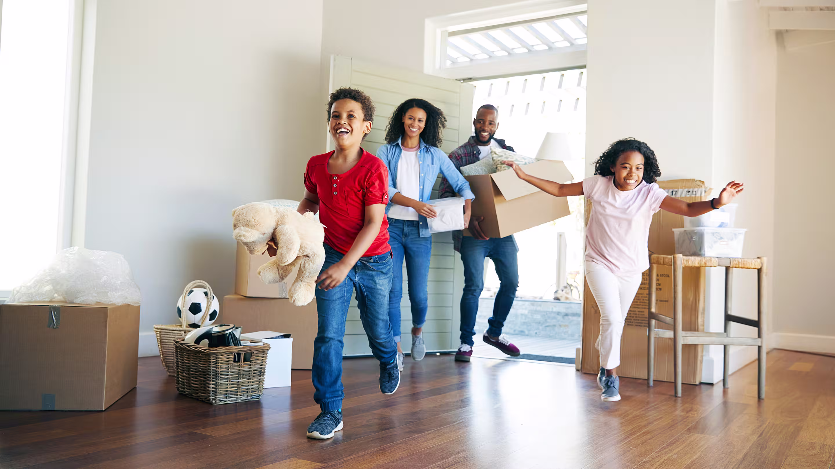 A joyful family with moving boxes enter into the bright living room of their recently purchased home.